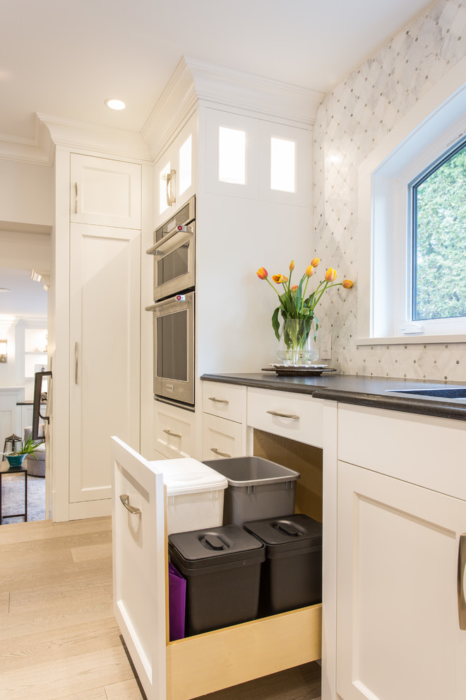 Large transitional l-shaped medium tone wood floor and beige floor eat-in kitchen photo in Vancouver with an undermount sink, shaker cabinets, white cabinets, granite countertops, gray backsplash, marble backsplash, stainless steel appliances, an island and black countertops