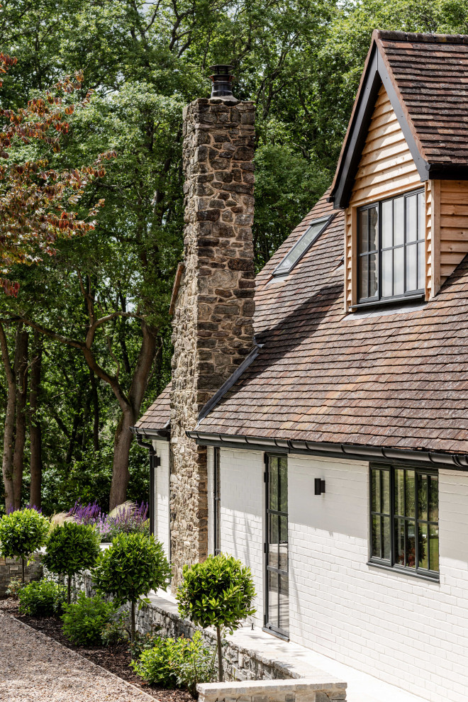 Photo of a large rural two floor front house exterior in Sussex with wood cladding, a pitched roof, a tiled roof, a red roof and board and batten cladding.