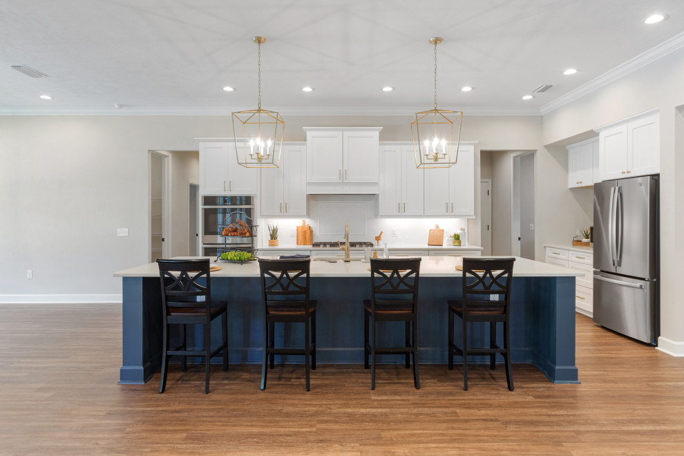 Inspiration for a mid-sized country l-shaped vinyl floor and brown floor open concept kitchen remodel in Other with shaker cabinets, white cabinets, quartzite countertops, white backsplash, ceramic backsplash, stainless steel appliances, an island, white countertops and an undermount sink