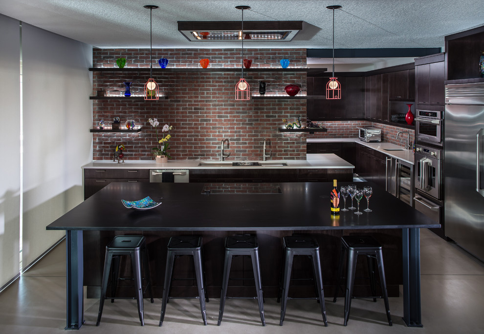 Example of an urban u-shaped concrete floor and gray floor kitchen design in Orlando with an undermount sink, flat-panel cabinets, dark wood cabinets, stainless steel appliances, an island and white countertops