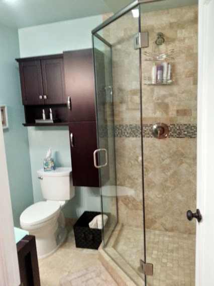 Cette image montre une petite salle de bain traditionnelle en bois foncé pour enfant avec un placard à porte plane, un plan de toilette en verre, une douche d'angle, WC séparés, un carrelage beige, un carrelage de pierre, un mur vert et un sol en travertin.