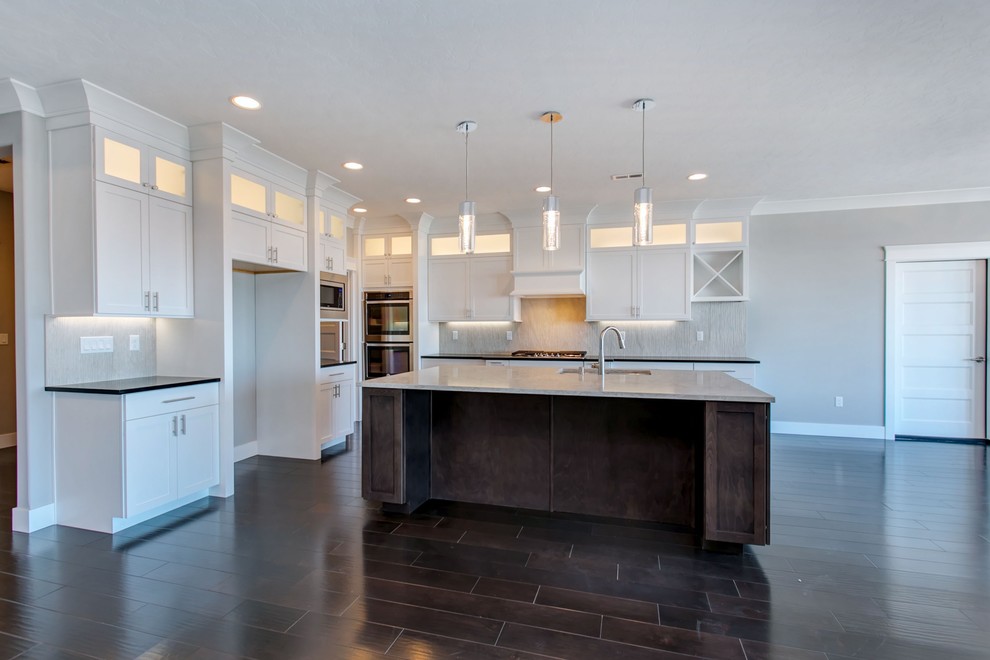 Open concept kitchen - large transitional l-shaped dark wood floor open concept kitchen idea in Seattle with an undermount sink, shaker cabinets, white cabinets, quartz countertops, gray backsplash, porcelain backsplash, stainless steel appliances, an island and white countertops