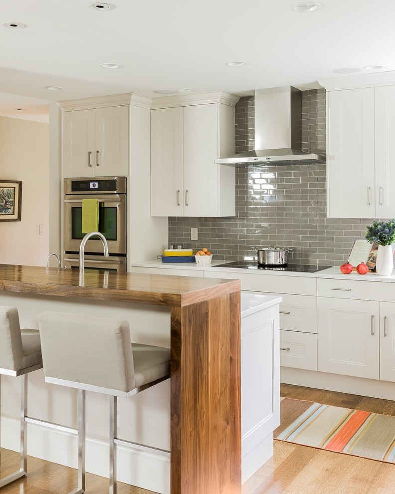 Design ideas for a large transitional galley eat-in kitchen in Boston with recessed-panel cabinets, white cabinets, grey splashback, subway tile splashback, stainless steel appliances, medium hardwood floors, with island and quartz benchtops.