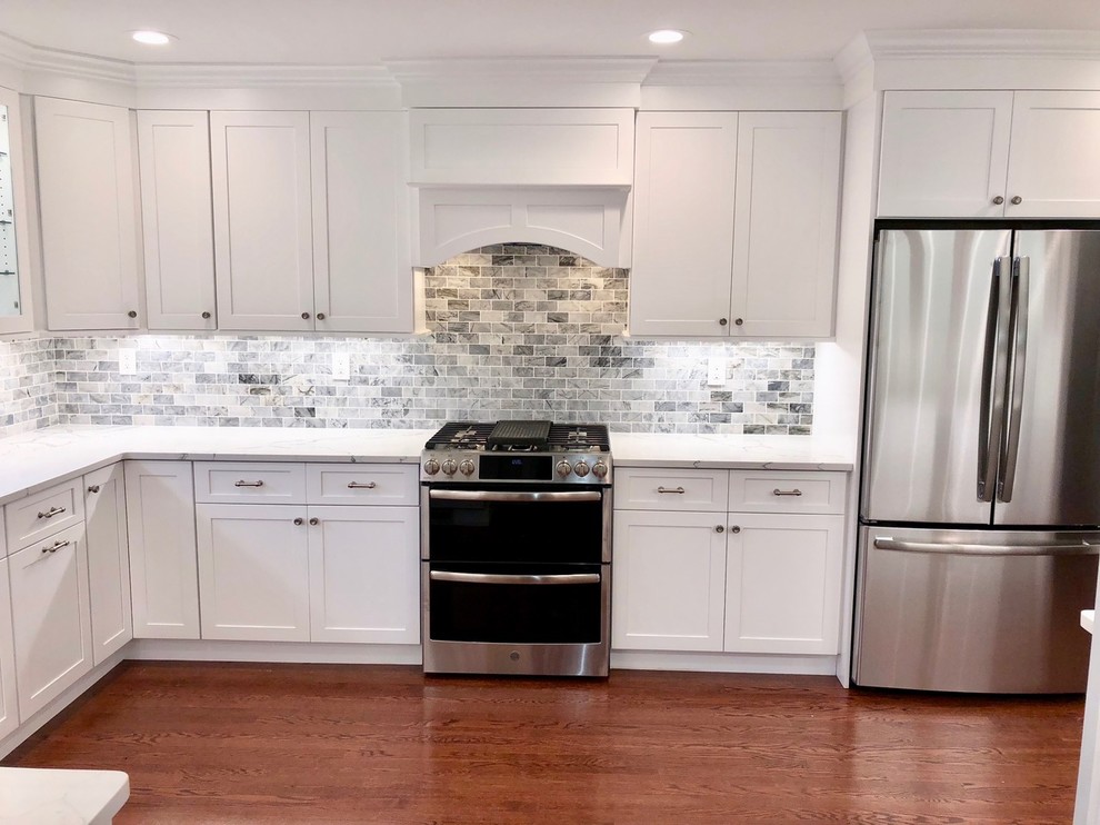 Example of a mid-sized transitional u-shaped dark wood floor and brown floor enclosed kitchen design with an undermount sink, shaker cabinets, white cabinets, marble countertops, gray backsplash, stone tile backsplash, stainless steel appliances, no island and white countertops