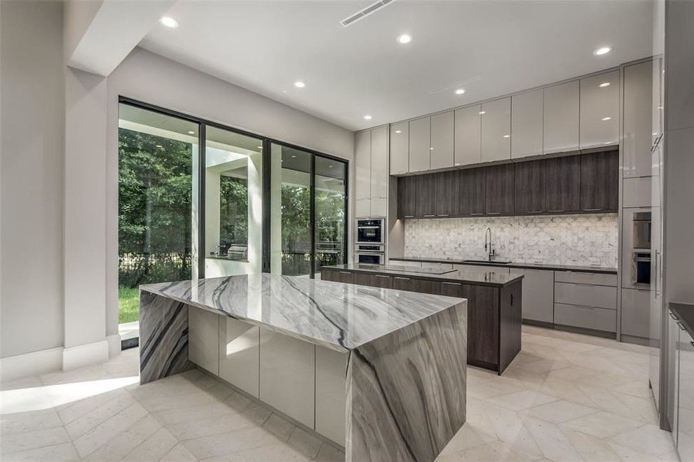 This is an example of a contemporary l-shaped open plan kitchen in Houston with flat-panel cabinets, grey cabinets, marble benchtops, grey splashback, marble splashback, stainless steel appliances, travertine floors, multiple islands, grey benchtop and grey floor.