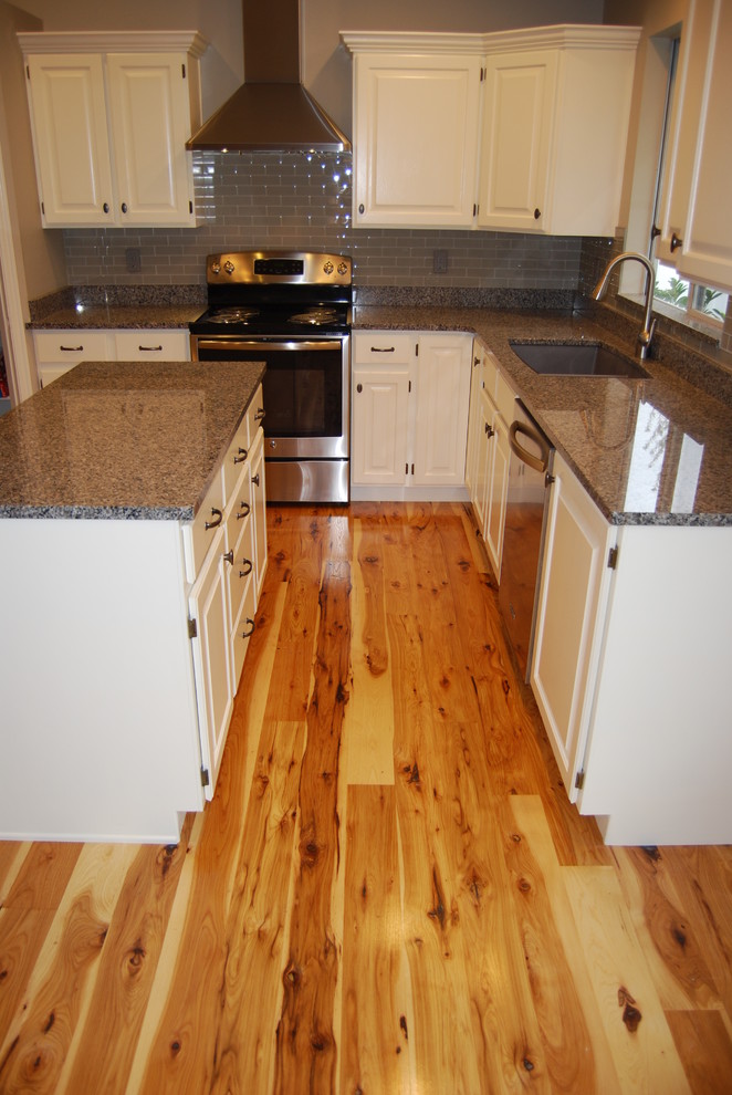 Example of a small transitional l-shaped light wood floor and brown floor eat-in kitchen design with a double-bowl sink, raised-panel cabinets, white cabinets, granite countertops, gray backsplash, stainless steel appliances, an island and glass tile backsplash