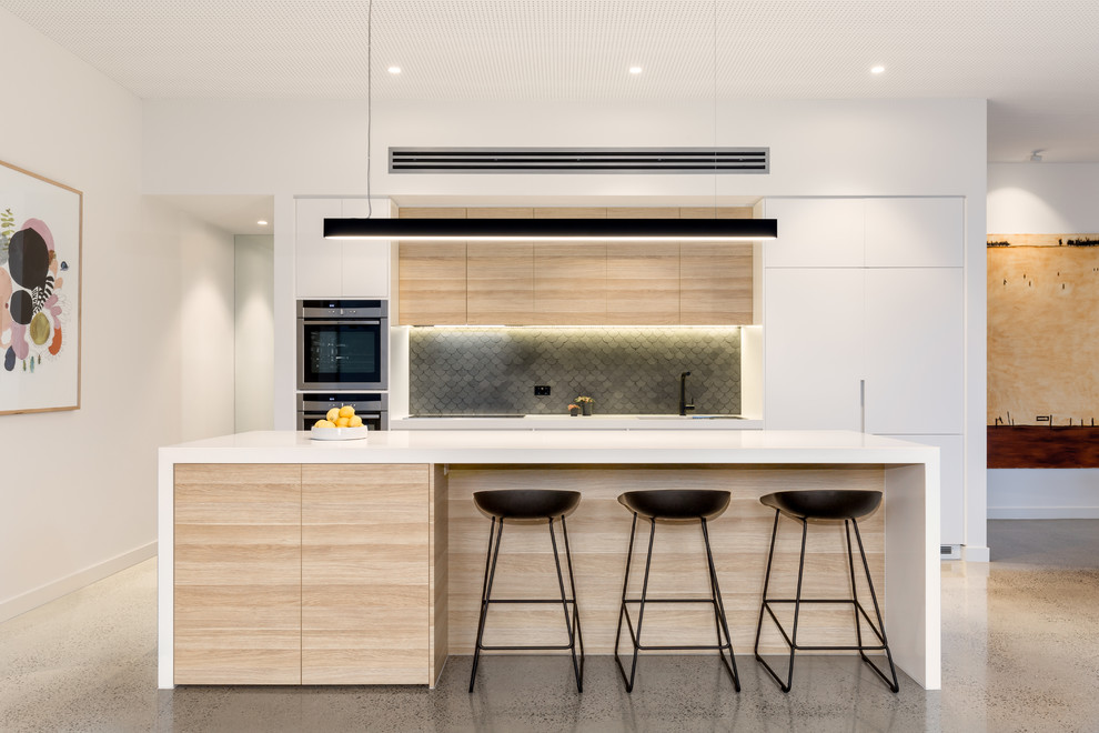 Design ideas for a mid-sized contemporary galley kitchen in Melbourne with an undermount sink, flat-panel cabinets, light wood cabinets, solid surface benchtops, grey splashback, stone tile splashback, stainless steel appliances and with island.