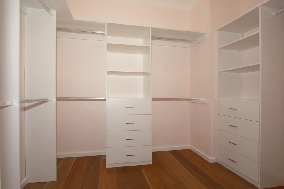 Mid-sized modern women's walk-in wardrobe in Melbourne with flat-panel cabinets, white cabinets and medium hardwood floors.