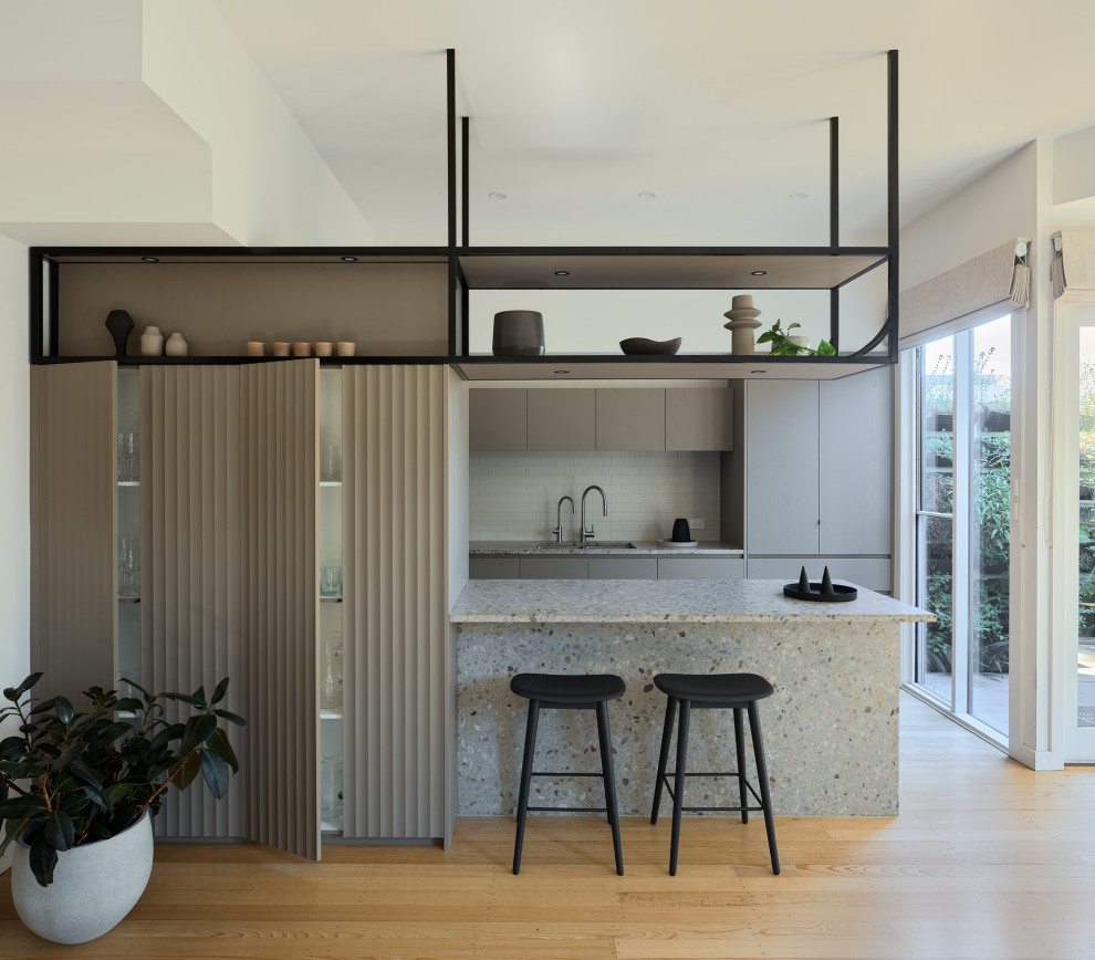 Photo of a small contemporary kitchen/diner in Melbourne with a double-bowl sink, flat-panel cabinets, grey cabinets, terrazzo worktops, grey splashback, ceramic splashback, black appliances, light hardwood flooring, an island and multicoloured worktops.