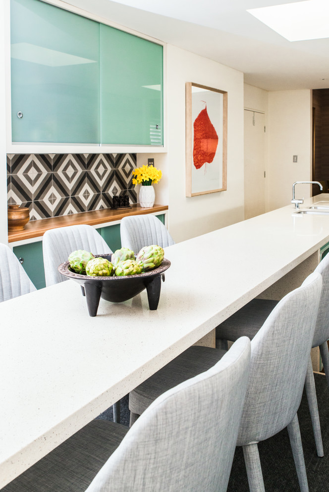 Mid-sized midcentury galley eat-in kitchen in Sydney with a double-bowl sink, glass-front cabinets, green cabinets, limestone benchtops, multi-coloured splashback, stone tile splashback, stainless steel appliances, light hardwood floors and with island.