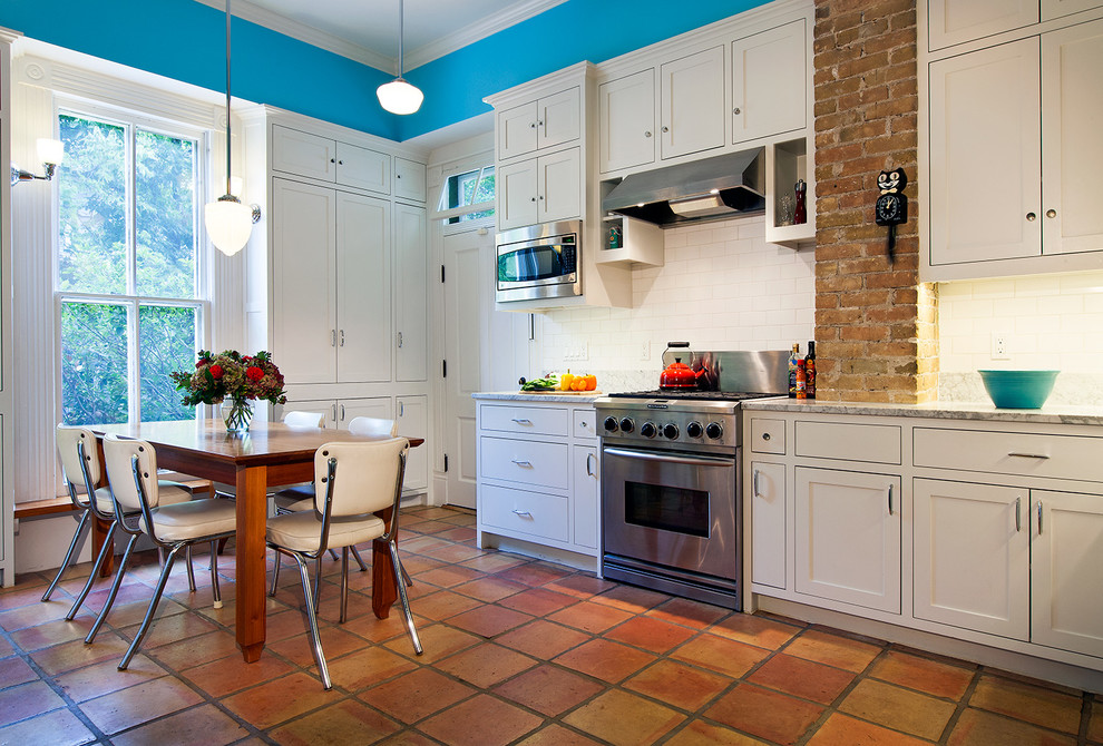 Example of an ornate galley terra-cotta tile eat-in kitchen design in Austin with a farmhouse sink, shaker cabinets, white cabinets, marble countertops, white backsplash, stainless steel appliances and subway tile backsplash