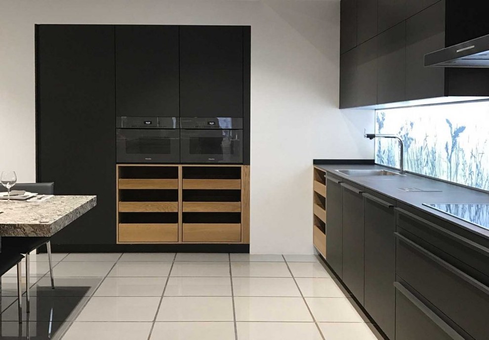 Photo of a mid-sized contemporary l-shaped open plan kitchen in Madrid with flat-panel cabinets, black cabinets, quartz benchtops, black appliances, porcelain floors, with island and grey floor.