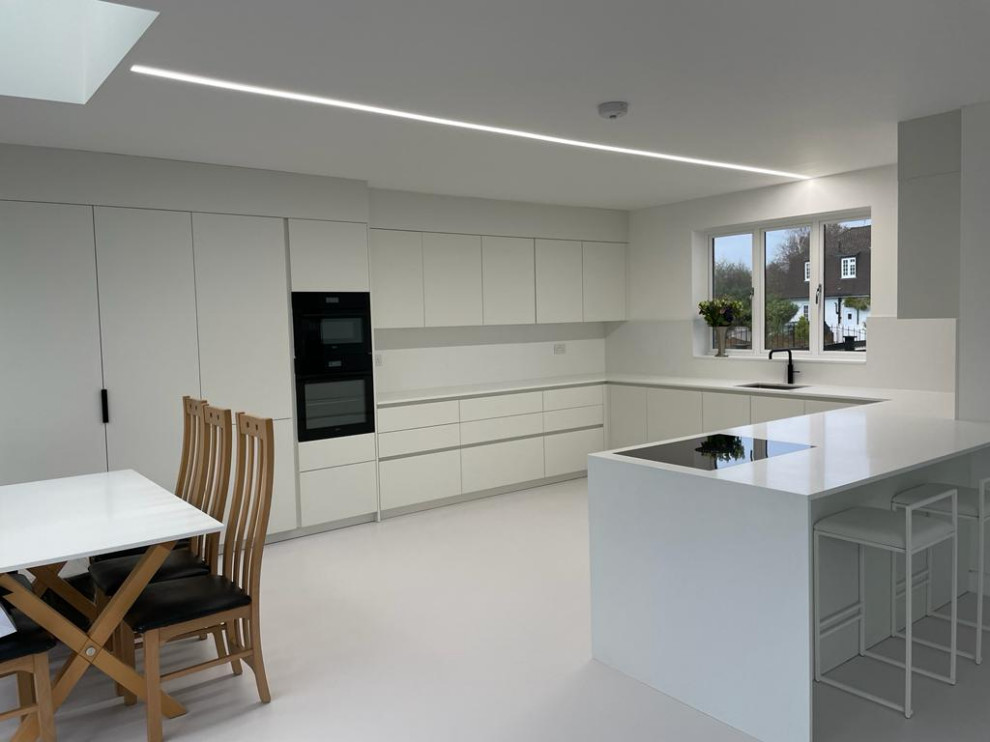 This is an example of a small contemporary u-shaped open plan kitchen in London with beaded cabinets, white cabinets, quartz worktops, white splashback, black appliances, white floors, white worktops, a coffered ceiling and feature lighting.