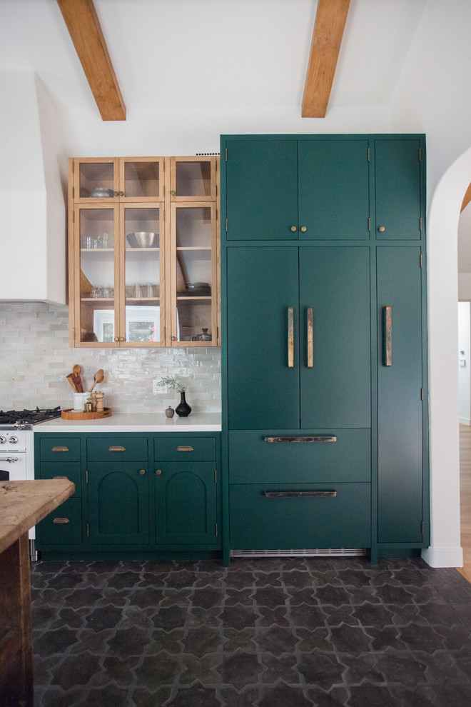Photo of a mid-sized mediterranean galley open plan kitchen in Los Angeles with flat-panel cabinets, green cabinets, quartz benchtops, white splashback, subway tile splashback, panelled appliances, ceramic floors, no island, black floor and white benchtop.