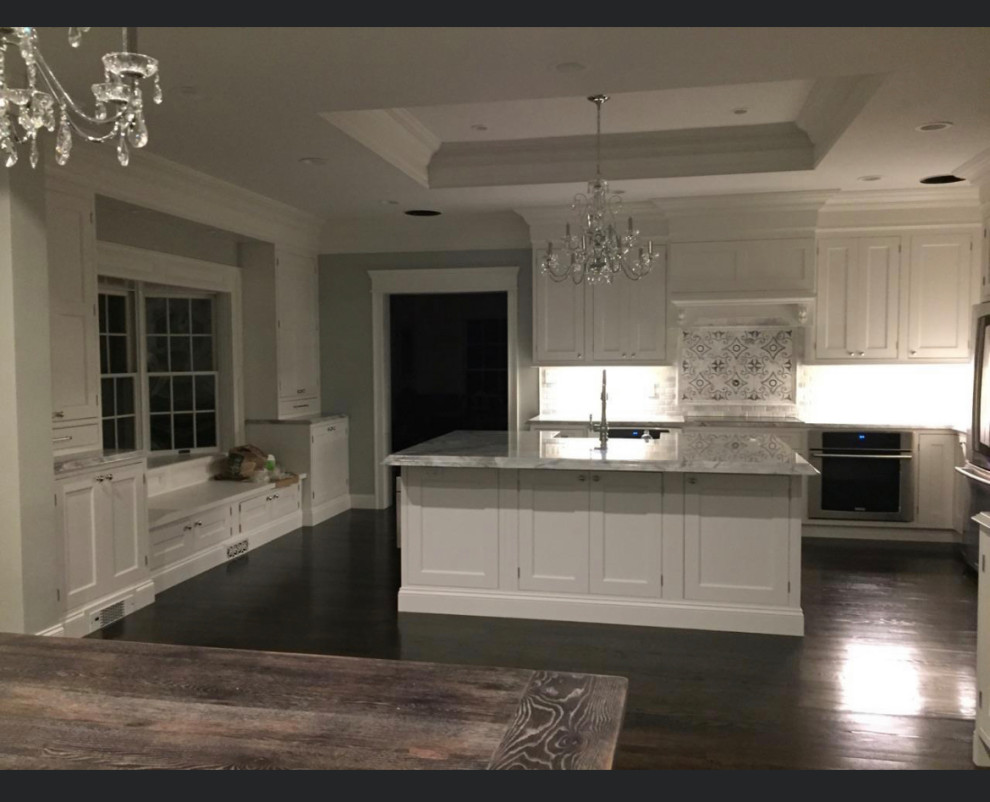 Inredning av ett klassiskt mycket stort grå grått kök, med en rustik diskho, luckor med profilerade fronter, vita skåp, bänkskiva i kvartsit, vitt stänkskydd, stänkskydd i marmor, rostfria vitvaror, mörkt trägolv, en köksö och brunt golv