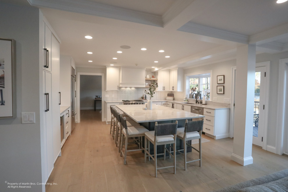 Example of a large transitional u-shaped light wood floor open concept kitchen design with an undermount sink, flat-panel cabinets, white cabinets, quartzite countertops, white backsplash, porcelain backsplash, stainless steel appliances, an island and white countertops