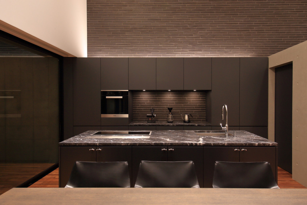 Modern galley open plan kitchen in Nagoya with a submerged sink, flat-panel cabinets, grey cabinets, black appliances, medium hardwood flooring, an island, brown floors and grey worktops.