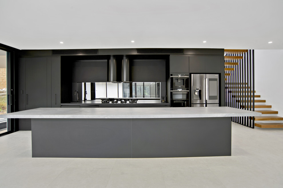 Imagen de cocina urbana grande con puertas de armario negras, encimera de cuarzo compacto, salpicadero con efecto espejo, una isla y encimeras grises