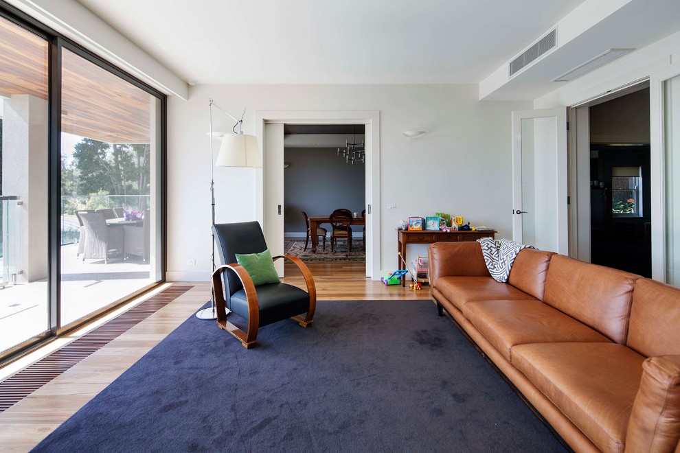 Photo of a large midcentury enclosed living room in Melbourne with light hardwood floors, white walls and no fireplace.