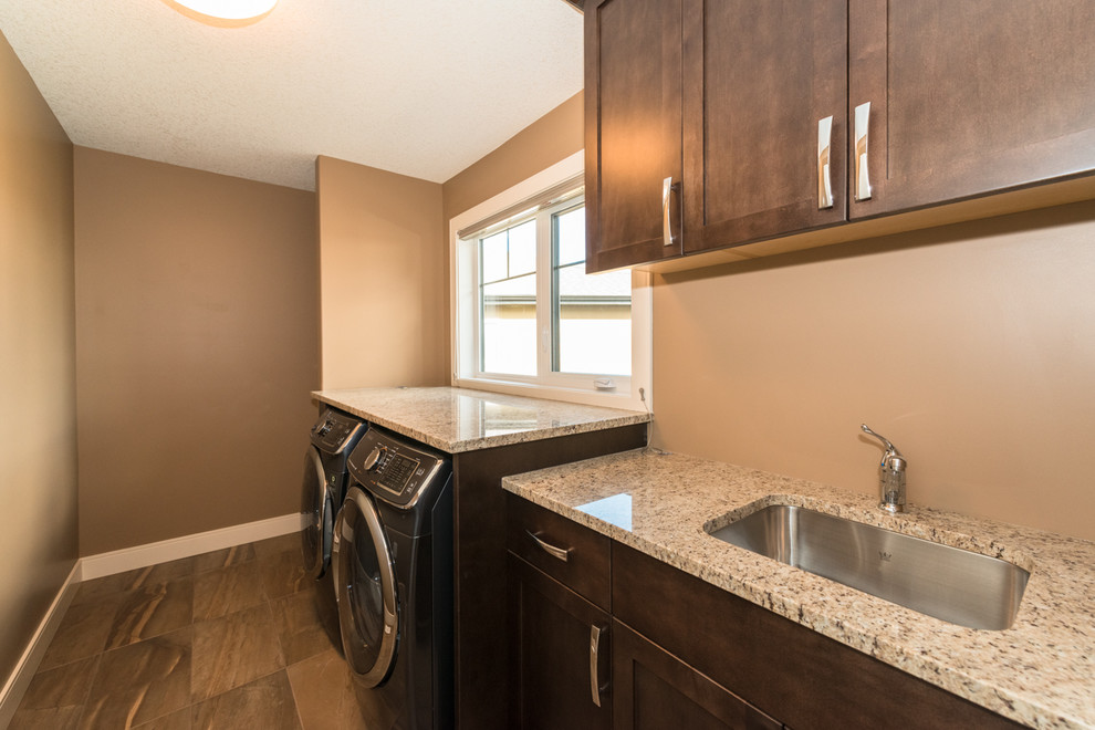 This is an example of a mid-sized contemporary single-wall dedicated laundry room in Edmonton with a single-bowl sink, recessed-panel cabinets, dark wood cabinets, granite benchtops, beige walls, ceramic floors and a side-by-side washer and dryer.