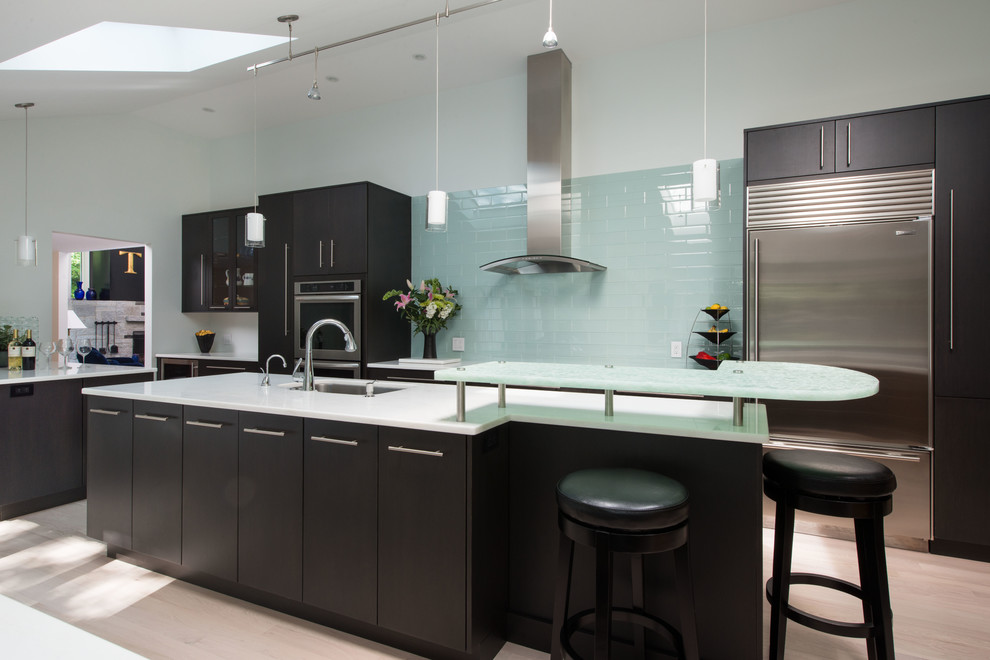 This is an example of a contemporary kitchen in Boston with stainless steel appliances, glass tile splashback, flat-panel cabinets, dark wood cabinets, an undermount sink, blue splashback and glass benchtops.