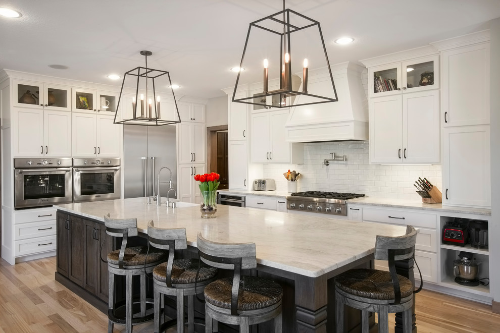 Design ideas for a traditional kitchen in Minneapolis with shaker cabinets, white cabinets, white splashback, subway tile splashback, stainless steel appliances, light hardwood floors, with island and beige floor.