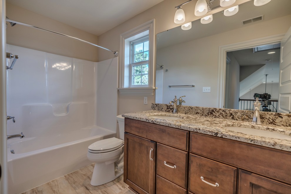 Tub/shower combo - large transitional kids' beige tile and ceramic tile ceramic tile and brown floor tub/shower combo idea with flat-panel cabinets, brown cabinets, a two-piece toilet, beige walls, an undermount sink, marble countertops, a hinged shower door and beige countertops