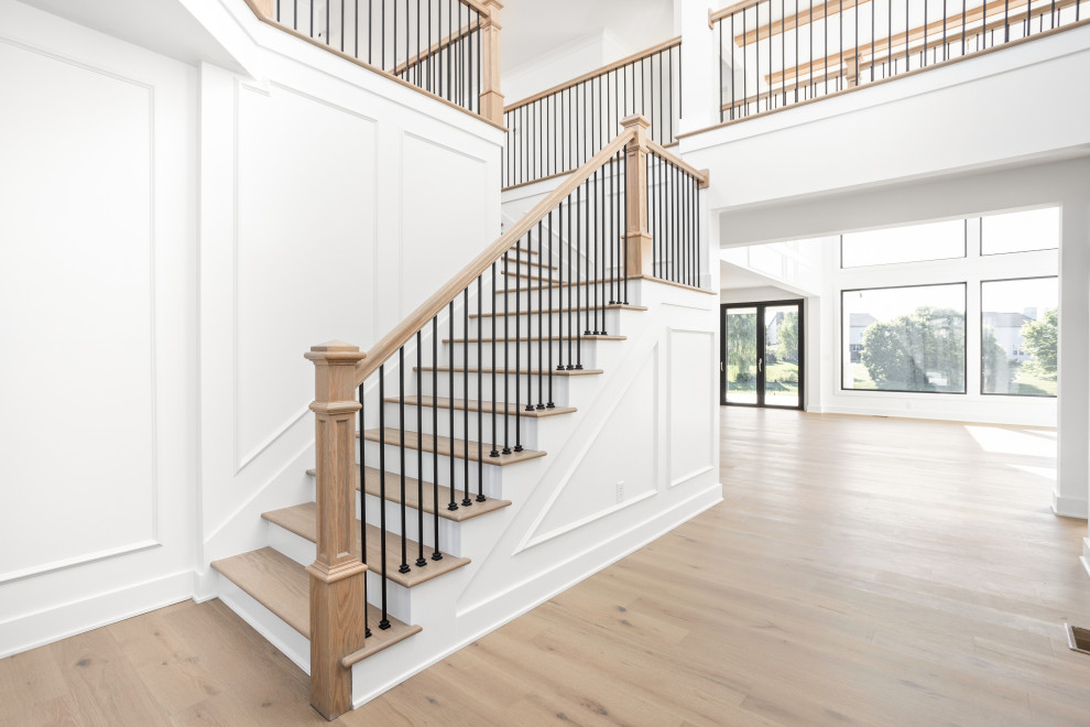 Стильный дизайн: большая угловая деревянная лестница в стиле неоклассика (современная классика) с деревянными ступенями, металлическими перилами и панелями на части стены - последний тренд