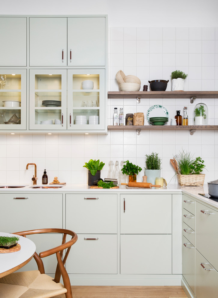 Mid-sized scandinavian l-shaped eat-in kitchen in Malmo with a double-bowl sink, flat-panel cabinets, green cabinets, white splashback, light hardwood floors, marble benchtops, ceramic splashback and no island.
