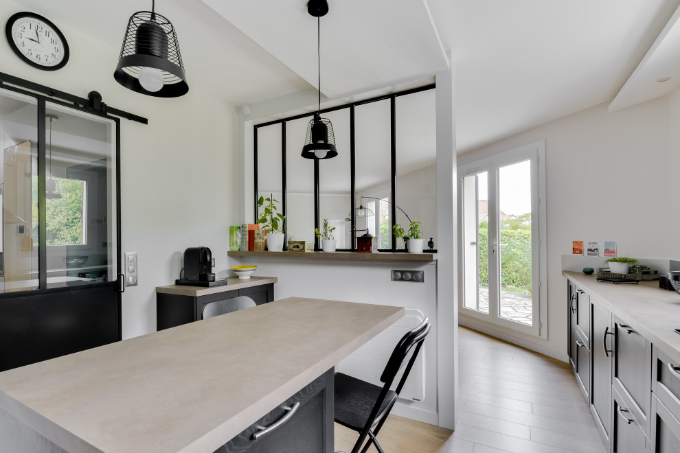 This is an example of a mid-sized industrial l-shaped open plan kitchen in Paris with an undermount sink, beaded inset cabinets, black cabinets, laminate benchtops, metallic splashback, metal splashback, stainless steel appliances, light hardwood floors, with island, beige floor and beige benchtop.