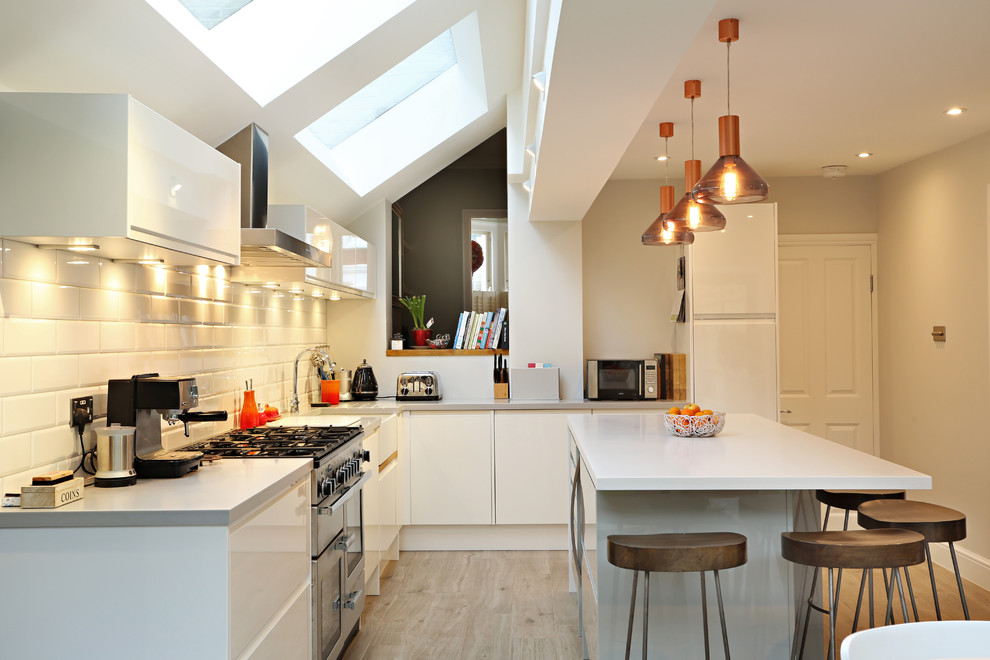 Inspiration for a transitional l-shaped kitchen in London with flat-panel cabinets, white cabinets, beige splashback, subway tile splashback and with island.