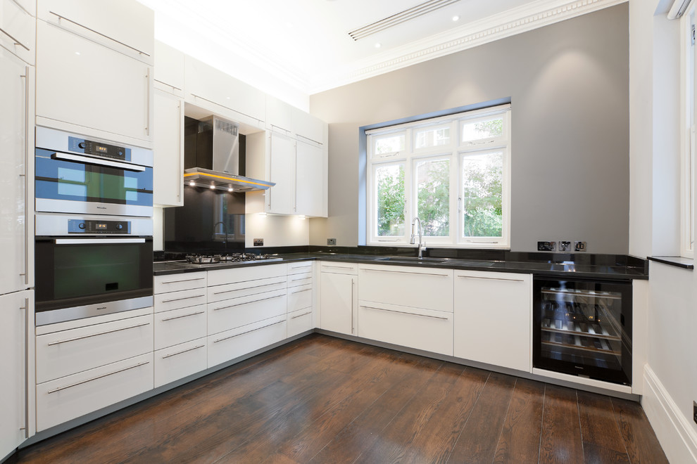 Inspiration for a mid-sized contemporary u-shaped separate kitchen in London with an undermount sink, flat-panel cabinets, black splashback, panelled appliances and dark hardwood floors.