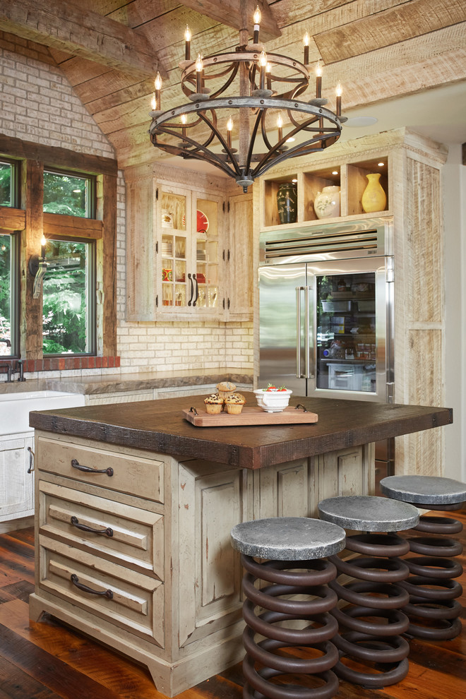 Design ideas for a mid-sized country u-shaped eat-in kitchen in Grand Rapids with a farmhouse sink, glass-front cabinets, distressed cabinets, concrete benchtops, beige splashback, brick splashback, stainless steel appliances, medium hardwood floors, with island and brown floor.