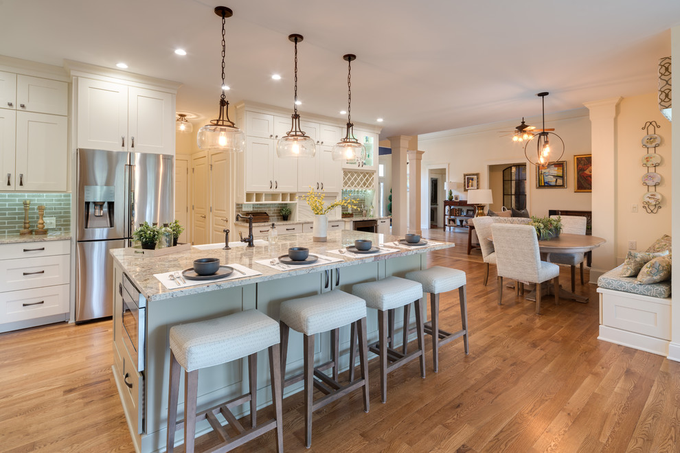 This is an example of a large traditional l-shaped eat-in kitchen in Atlanta with a farmhouse sink, shaker cabinets, white cabinets, granite benchtops, subway tile splashback, stainless steel appliances, medium hardwood floors, with island, brown floor, beige benchtop and brown splashback.