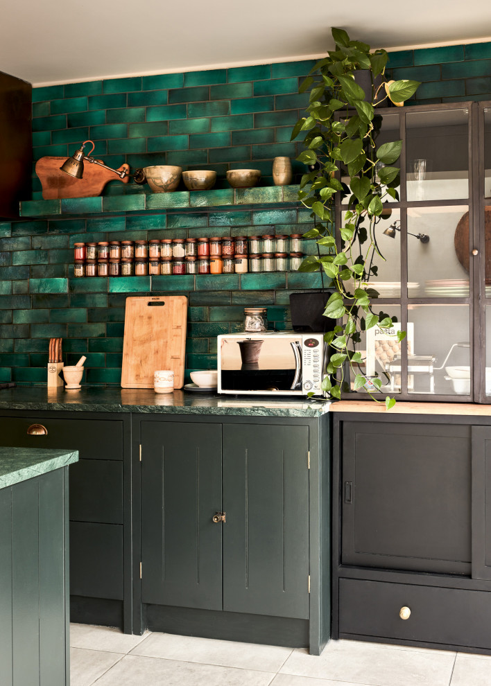 This is an example of a mid-sized single-wall eat-in kitchen in London with a drop-in sink, glass-front cabinets, black cabinets, marble benchtops, green splashback, ceramic splashback, panelled appliances, ceramic floors, with island, grey floor and green benchtop.