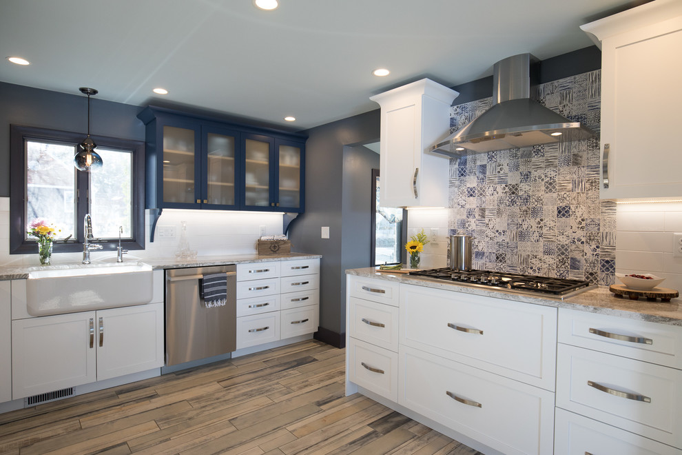 Photo of a mid-sized beach style l-shaped open plan kitchen in Manchester with a farmhouse sink, shaker cabinets, blue cabinets, glass benchtops, yellow splashback, ceramic splashback, painted wood floors and multi-coloured floor.