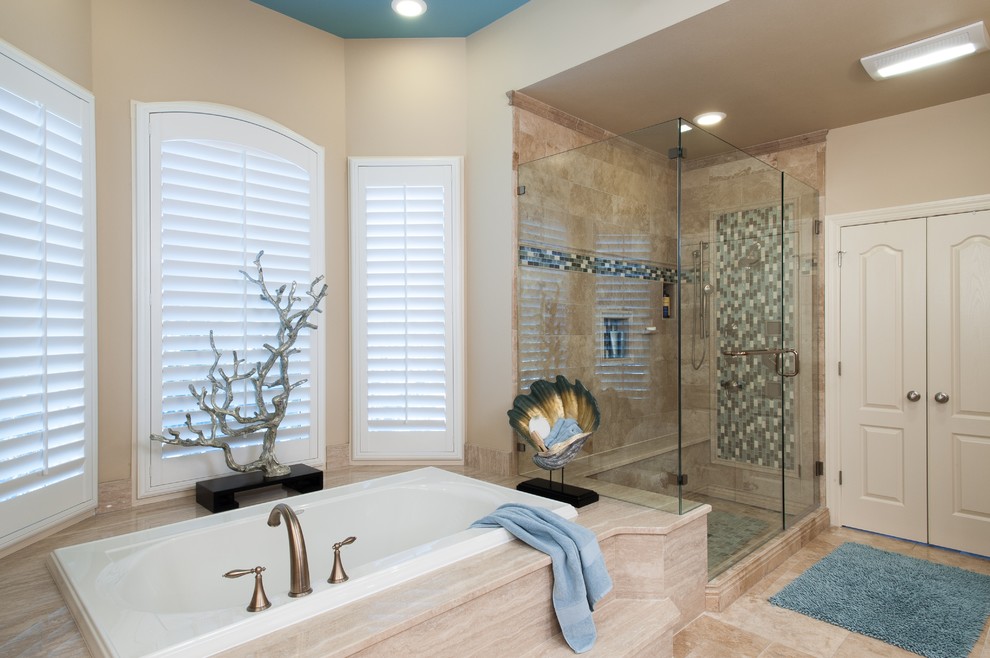 Inspiration for a large transitional master bathroom in St Louis with furniture-like cabinets, medium wood cabinets, a drop-in tub, a double shower, a one-piece toilet, beige tile, travertine, blue walls, limestone floors, an undermount sink, limestone benchtops, beige floor and a hinged shower door.