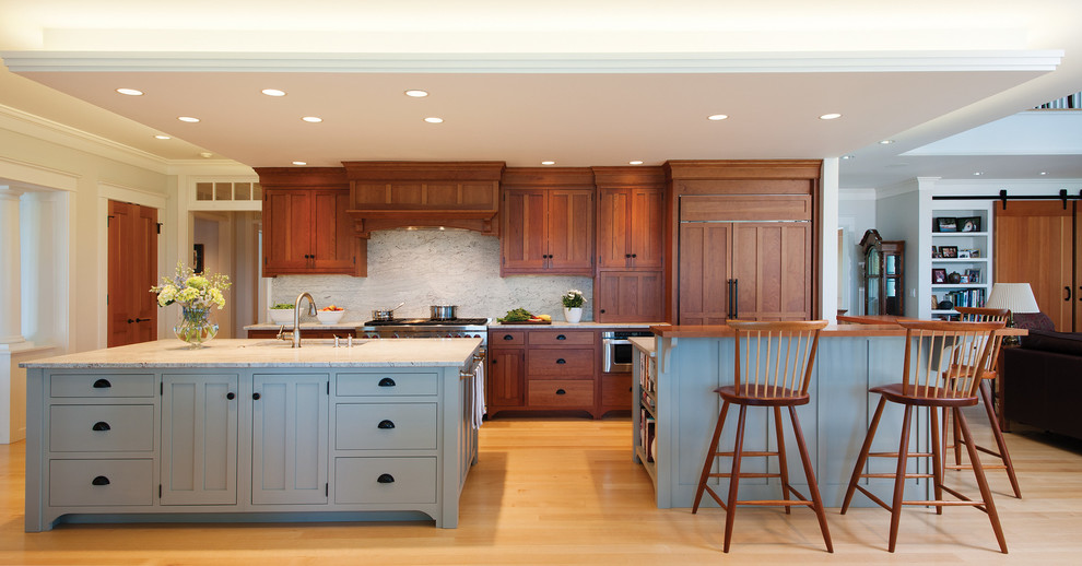 Large arts and crafts single-wall eat-in kitchen in Portland Maine with medium wood cabinets, granite benchtops, stone slab splashback, light hardwood floors, multiple islands, a single-bowl sink, shaker cabinets, white splashback and stainless steel appliances.