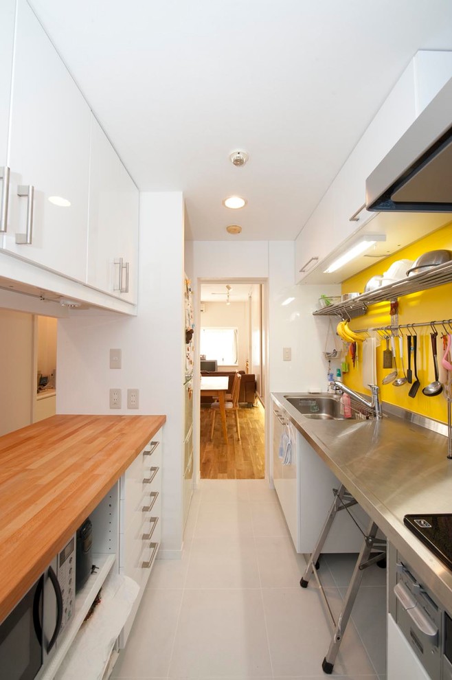 Photo of an industrial single-wall separate kitchen in Tokyo with a single-bowl sink, flat-panel cabinets, white cabinets, stainless steel benchtops, yellow splashback, a peninsula, grey floor and brown benchtop.