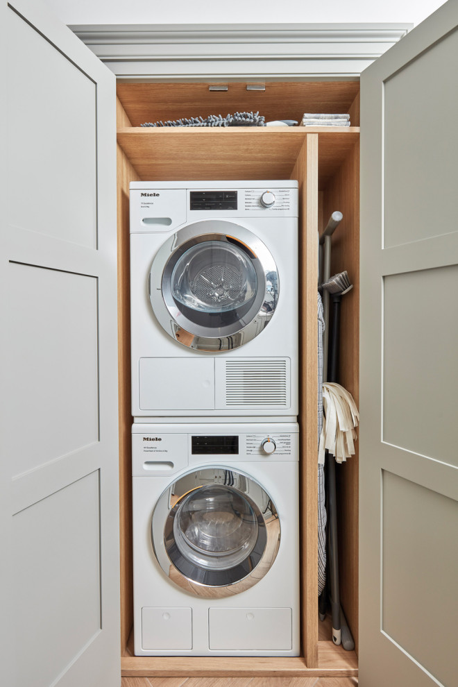 This is an example of a small traditional laundry room in Hertfordshire with shaker cabinets, grey cabinets, quartz benchtops, white splashback, engineered quartz splashback, white walls, porcelain floors, a stacked washer and dryer, beige floor, white benchtop and panelled walls.