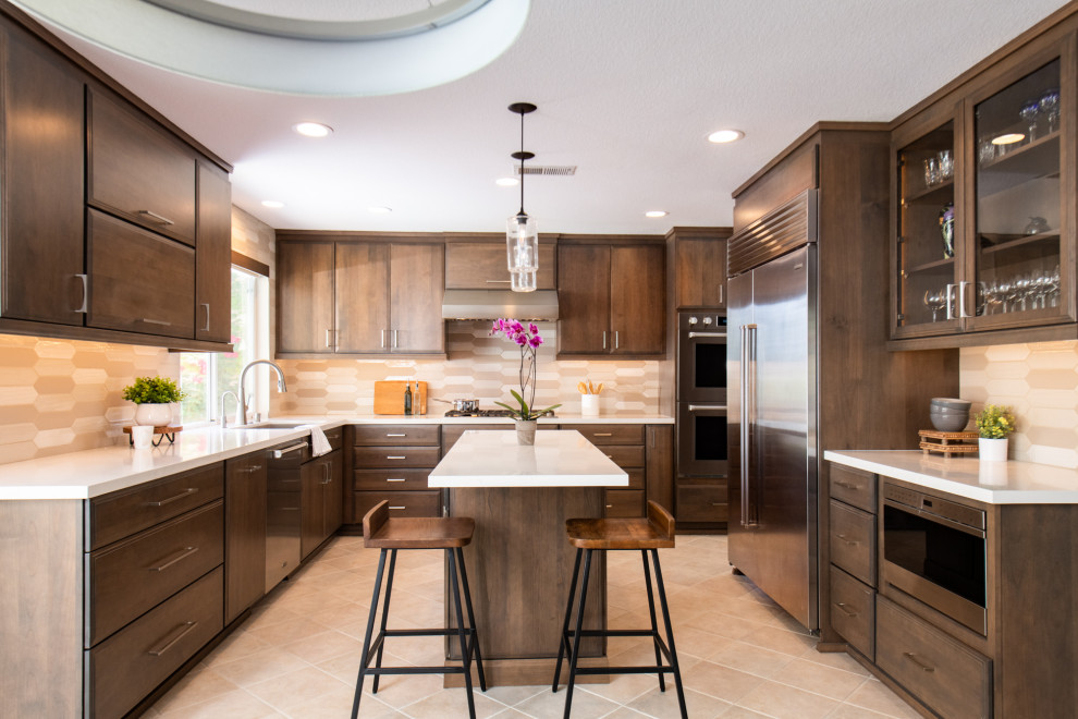 Photo of a medium sized traditional u-shaped kitchen/diner in Orange County with shaker cabinets, brown cabinets, engineered stone countertops, beige splashback, porcelain splashback, stainless steel appliances, an island and white worktops.