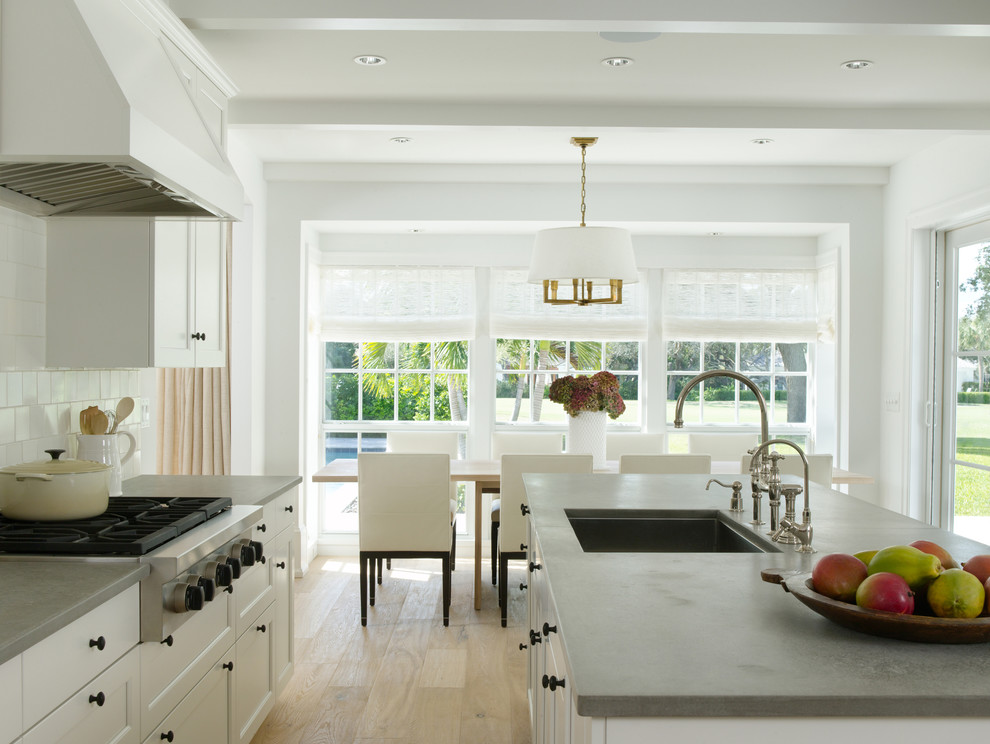 This is an example of a tropical eat-in kitchen in Miami with white cabinets, white splashback and an undermount sink.