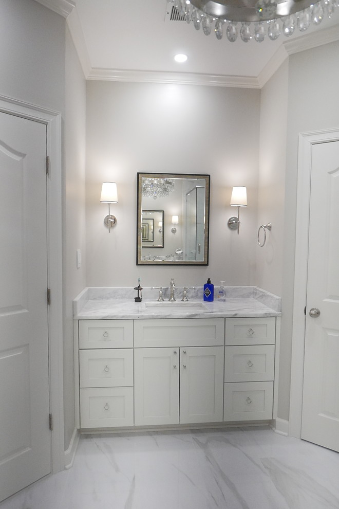 Example of a large transitional master white tile and porcelain tile porcelain tile and white floor freestanding bathtub design with shaker cabinets, white cabinets, a two-piece toilet, beige walls, an undermount sink, marble countertops, a hinged shower door and white countertops