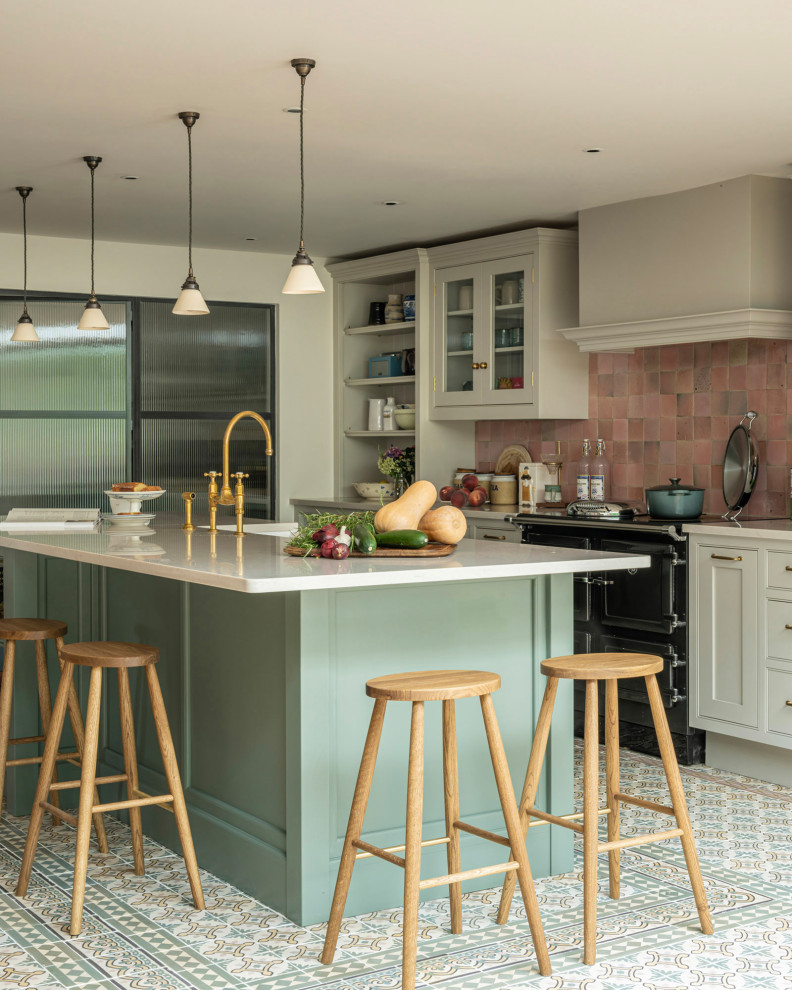 Transitional ceramic tile eat-in kitchen photo in Buckinghamshire with a farmhouse sink, shaker cabinets, green cabinets, solid surface countertops, pink backsplash, ceramic backsplash, black appliances, an island and white countertops