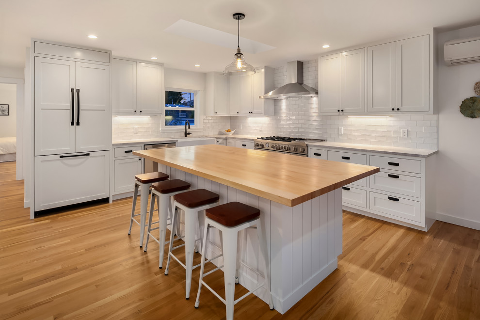 Inspiration for a mid-sized arts and crafts kitchen in Seattle with a farmhouse sink, shaker cabinets, white cabinets, quartzite benchtops, white splashback, subway tile splashback, stainless steel appliances, light hardwood floors, with island and grey benchtop.