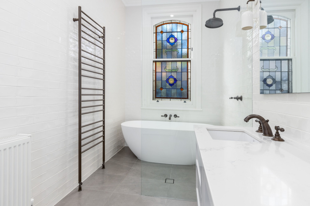 This is an example of a mid-sized transitional master wet room bathroom in Melbourne with shaker cabinets, white cabinets, a freestanding tub, white tile, subway tile, white walls, porcelain floors, an undermount sink, engineered quartz benchtops, grey floor, an open shower, white benchtops, a double vanity and a floating vanity.