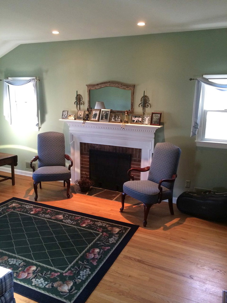 Photo of a traditional enclosed living room in New York with green walls, light hardwood floors, a standard fireplace and a wood fireplace surround.