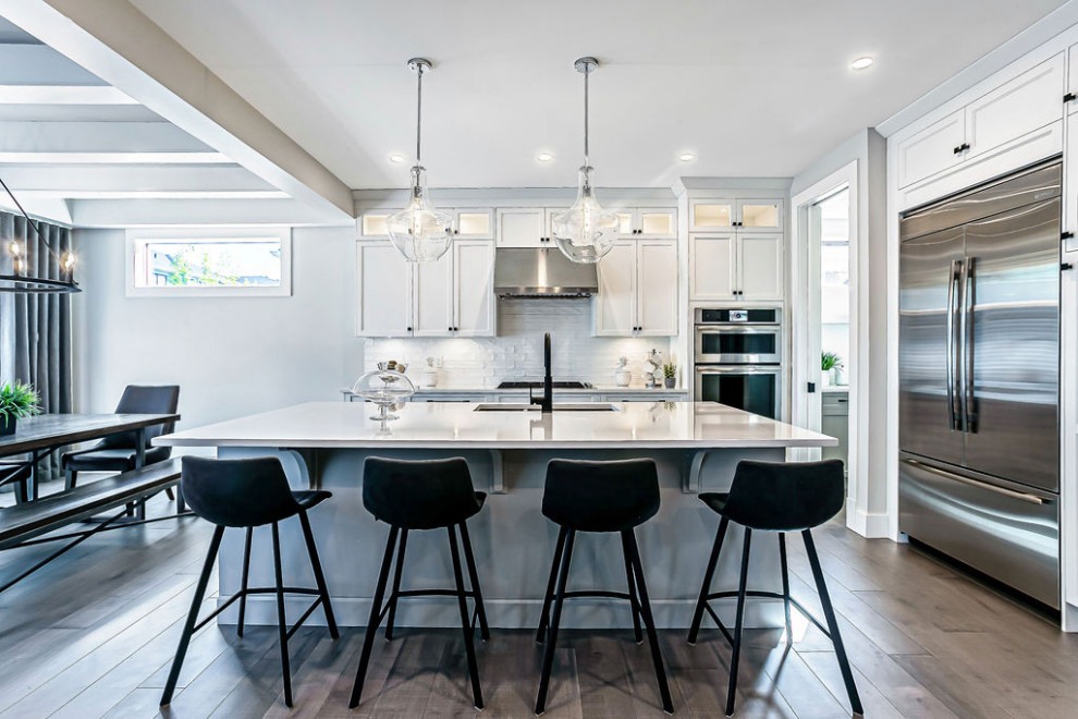 Example of a transitional l-shaped light wood floor and gray floor eat-in kitchen design in Calgary with a double-bowl sink, shaker cabinets, gray cabinets, quartz countertops, white backsplash, ceramic backsplash, stainless steel appliances, an island and white countertops