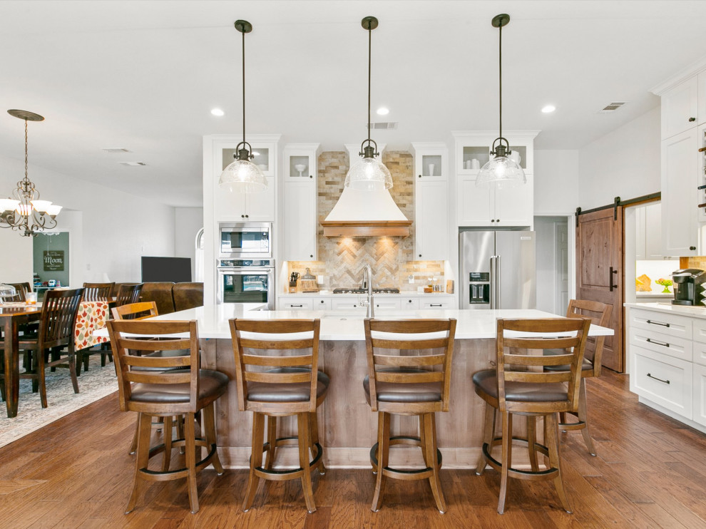 Photo of a country l-shaped kitchen in Dallas with an undermount sink, shaker cabinets, white cabinets, beige splashback, medium hardwood floors, with island, brown floor and white benchtop.