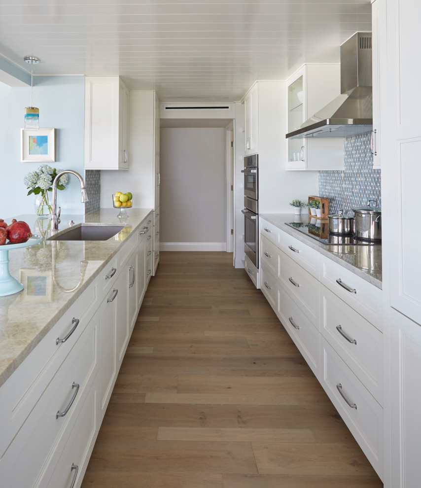 Design ideas for a mid-sized beach style galley open plan kitchen with an undermount sink, shaker cabinets, white cabinets, quartzite benchtops, multi-coloured splashback, glass tile splashback, panelled appliances, medium hardwood floors, a peninsula, brown floor, grey benchtop and timber.